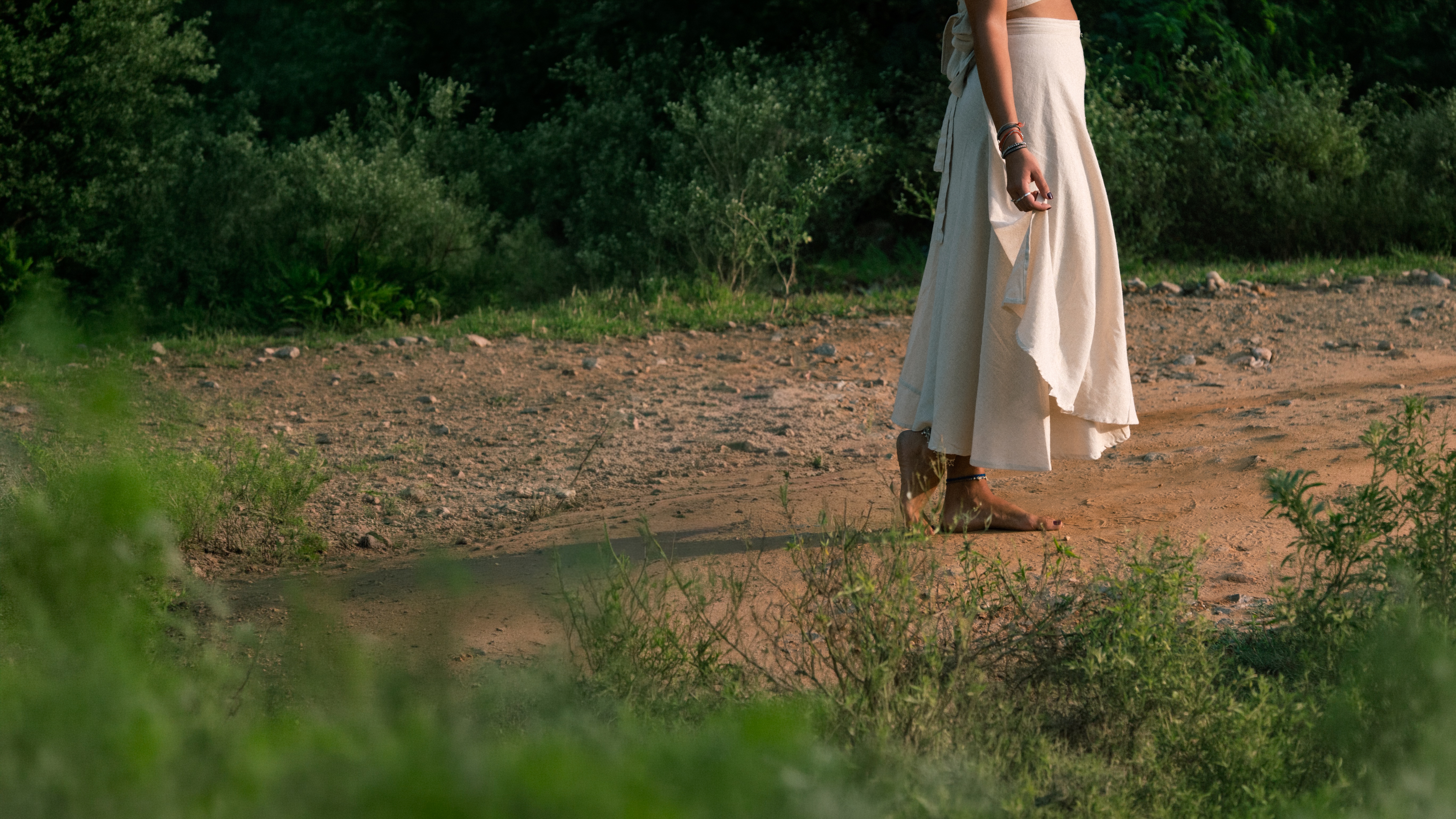 A woman wearing a flowing cream LAYA wrap skirt on a dirt path in Rajasthan, India.